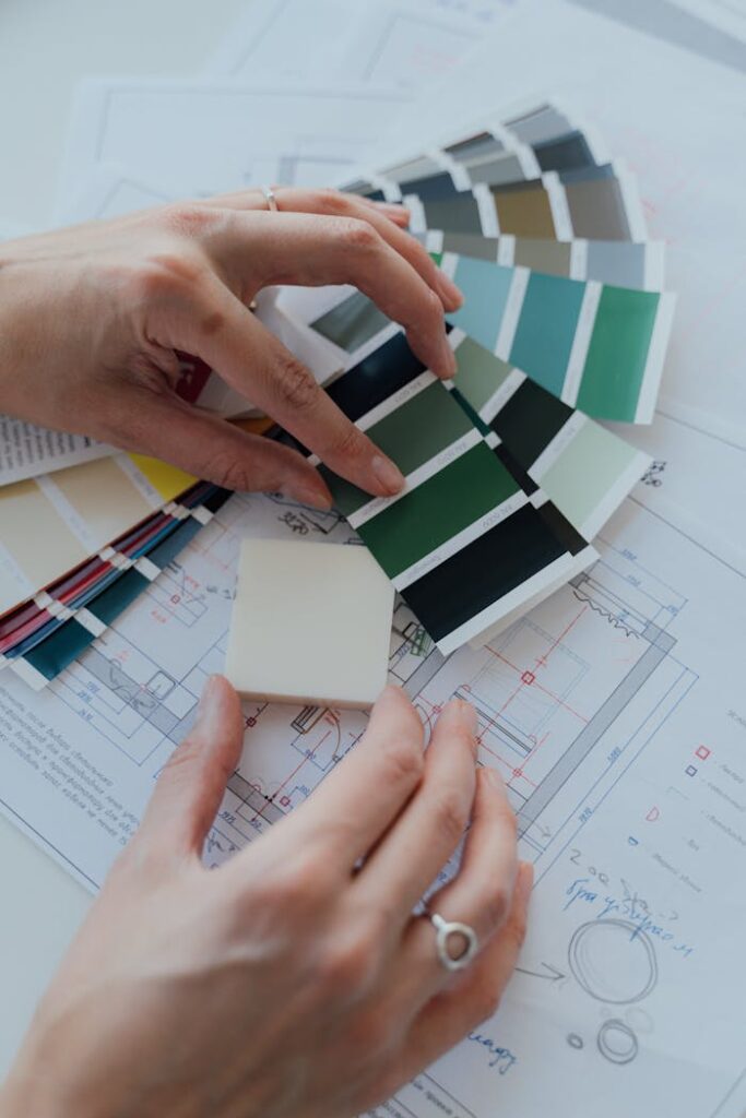 Hands selecting color samples over architectural plans for interior design.